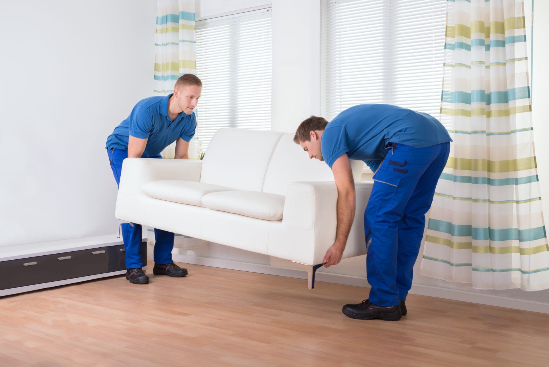 Full length of male movers placing sofa on hardwood floor at home